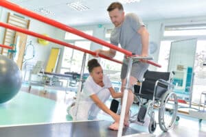 Patient qui marche entre deux barres fixes avec une thérapeute